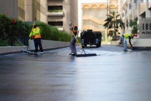 workers slurry sealing the pavement between two buildings